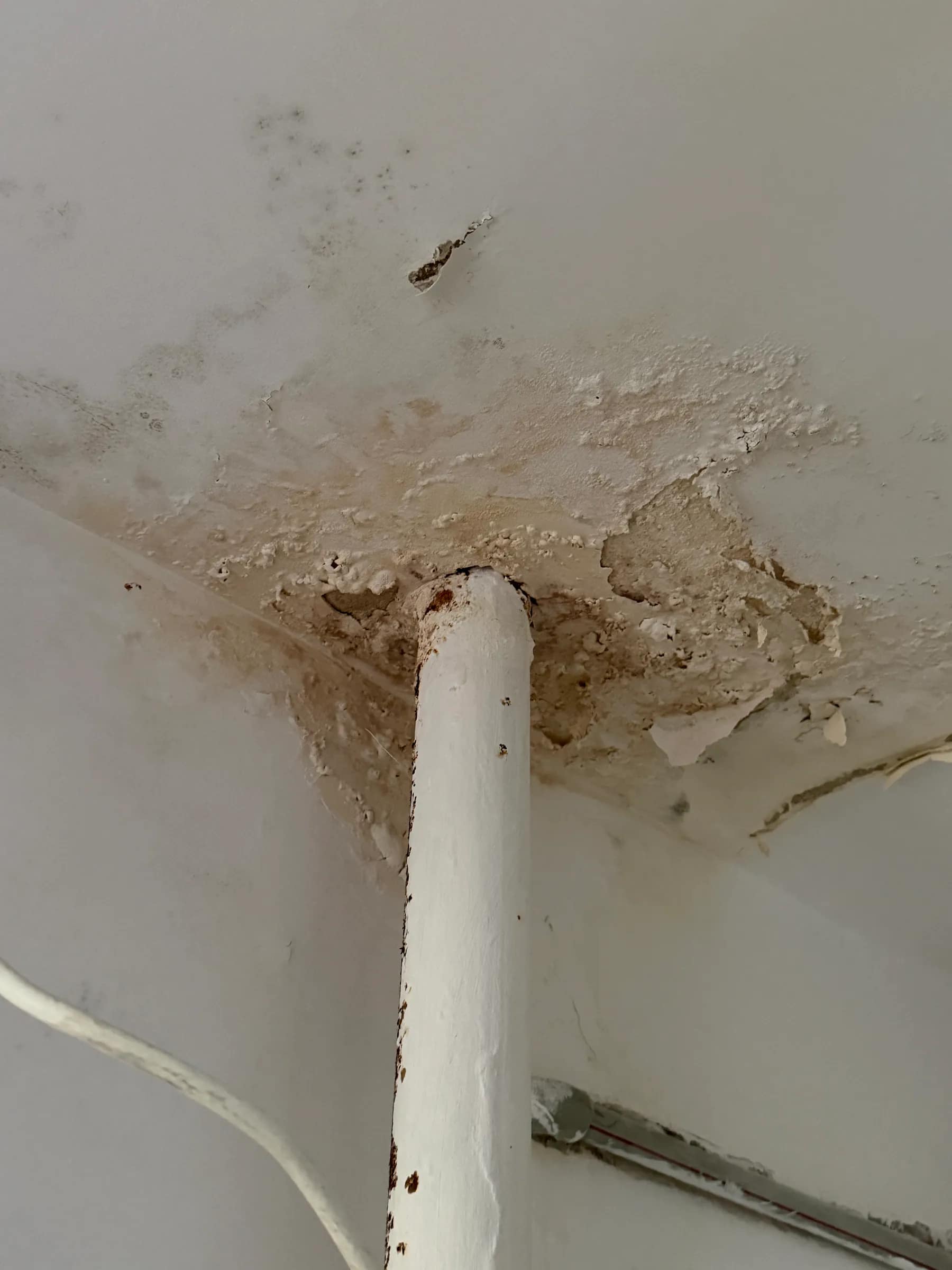 Zawilgocony i odspojony tynk na suficie przy przejściu instalacyjnym