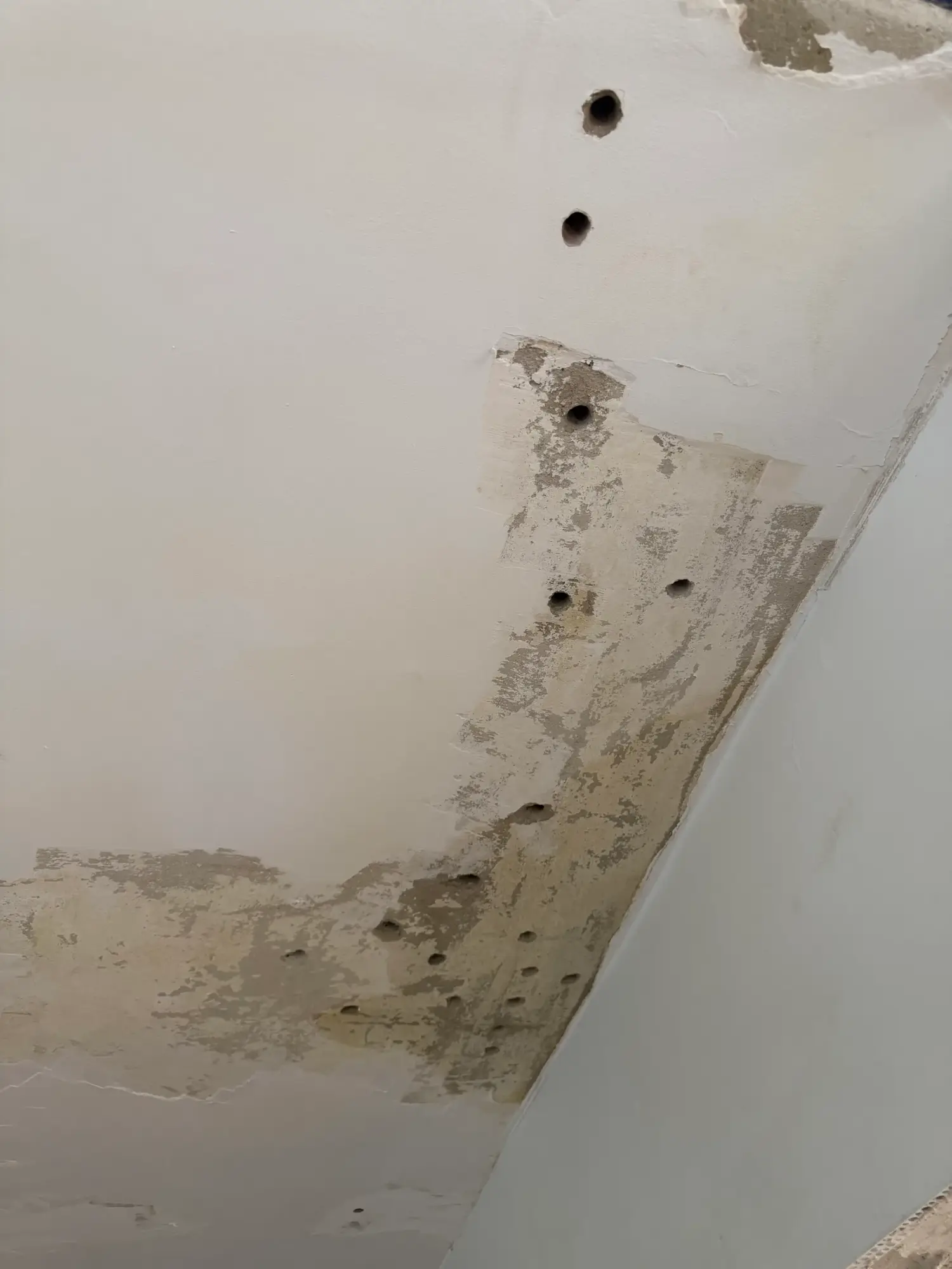 Uszkodzony tynk i otwory w suficie przy narożniku pomieszczenia